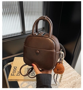 Detail view of a vintage dark brown PU leather mini bag with bear charm and top handle