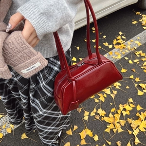 Deep red patent leather Boston bag with long straps on autumn ginkgo leaves background