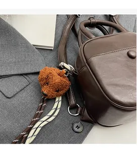 Detail of dark brown leather backpack with teddy bear charm on grey suit fabric