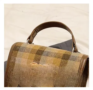 Detail showing the brown plaid fabric, cute bear patch, and leather handle of the backpack