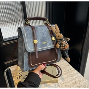 Detailaufnahme von grauem Denim-Rucksack mit braunem Leder und niedlichem Hasenanhänger