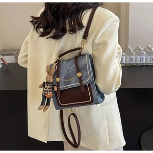 Detail eines blauen Denim-Leder-Rucksacks mit brauner Klappe und süßem Hasenanhänger