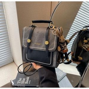 Details von grauem Stoff und schwarzem Lederrucksack mit goldener Taste und Hasenanhänger
