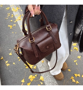 Detail of a dark brown Boston bag with vintage texture and gold hardware in an autumn setting