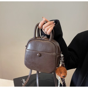 Detail of dark brown faux leather bag featuring a cute teddy bear plush charm and top handle
