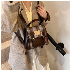 Detail of retro plaid crossbody bag with bear patch shown on a model in beige suit