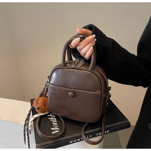Detail of dark brown mini square bag with metal zipper and plush bear charm decoration