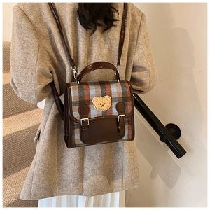 Detail of plaid backpack featuring brown leather trim and cute teddy bear patch