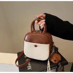 Detail of a brown and beige crossbody bag with double zippers and a plush bear charm