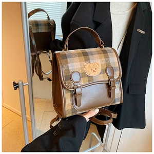 Detail view of the vintage plaid flap and cute cartoon bear patch on the brown leather bag
