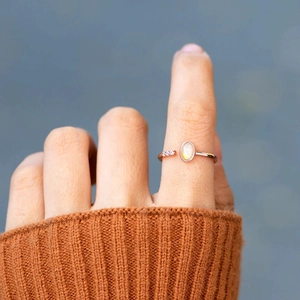 Close-up of rose gold opal ring with oval stone and side zircon accents on a finger