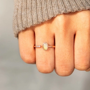 Close-up of rose gold opal ring with three side diamonds worn on a finger