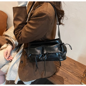 Detail of black glossy shoulder bag with dual front pockets and decorative drawstrings