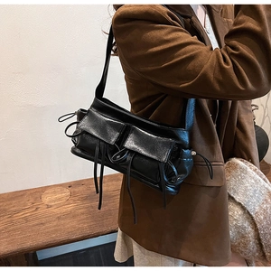 Detail of black faux leather shoulder bag featuring double front pockets and long tassels