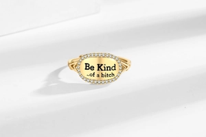Detail of gold letter ring featuring Be Kind engraving and sparkling crystal border