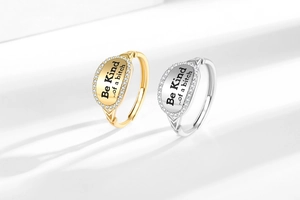 Detailed view of gold and silver oval rings with Be Kind lettering and pavé crystals