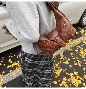 Détail du sac en cuir marron avec rivets métalliques et boucles sur feuilles d'automne