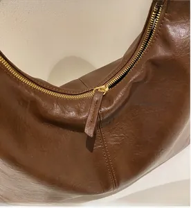 Close-up of golden zipper and oily polished leather texture on dark brown hobo bag