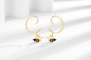 Détail de boucles d'oreilles abeille dorées avec design unique en spirale en C sur blanc