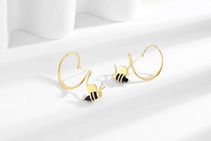 Détail de boucles d'oreilles abeille dorées avec rayures en émail noir sur fond blanc