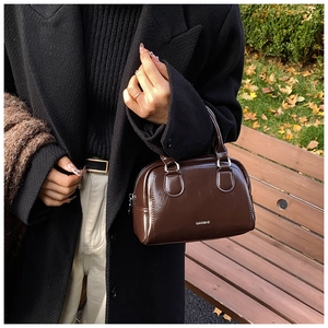 Detailed view of a dark brown oil wax leather Boston bag held by a model in a wool coat
