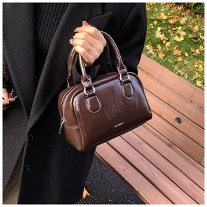 Detail of dark brown glossy leather bowling bag held by a model in an outdoor park
