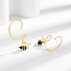 Boucles d'oreilles abeille dorées avec détails en émail noir sur fond blanc épuré