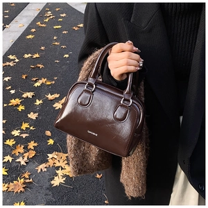 Close-up of a dark brown oil wax leather Boston bag with white brand logo in autumn setting
