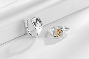 Detail view of two silver and gold rose floral relief square signet rings on a white step