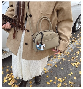 Detail of a chic beige square handbag with dual handles and a blue horse charm pendant