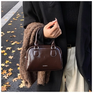 Dark coffee glossy leather bowling bag and brown wool scarf on autumn street