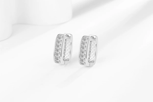 Macro shot of silver U-shaped hoop earrings with baguette-cut zircons and hollow grid design