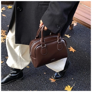 Deep brown leather bowling bag with silver zipper on a wooden bench with maple leaves