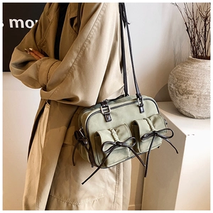 Detail of sage green suede shoulder bag featuring two front pockets and black ribbon bows