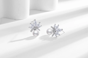 Detail of silver pearl stud earrings with marquise cubic zirconia and crown floral accents