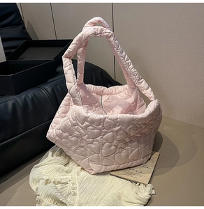 Detail of light pink quilted tote bag featuring padded heart patterns and secure zipper closure