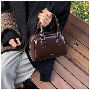 Detailed top view of a dark brown oil wax leather Boston bag with glossy finish on a bench
