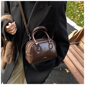 Close-up of a dark brown glossy leather bowling bag with detachable shoulder strap and handles
