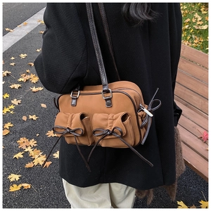 Macro detail of brown suede shoulder bag featuring decorative leather bow pockets