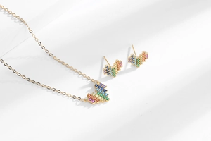 Macro detail of gold rainbow pixel heart necklace and stud earrings set with zircon