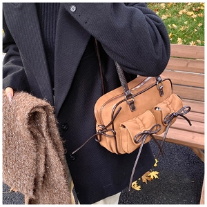 Detail of brown suede shoulder bag with front pockets and decorative leather bows