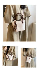 Detalle de bolso bucket de cuero crema con asas marrones y accesorio colgante tejido