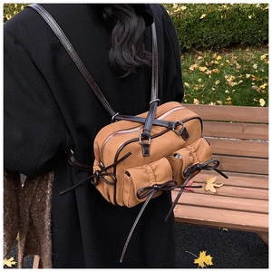 Close-up of khaki shoulder bag with bow details and brown straps in autumn park