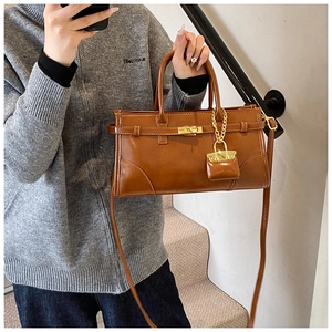 Detail einer braunen Ledertasche mit goldener Schließe und einem Mini-Taschenanhänger