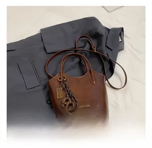 Detalle de bolso bucket de cuero marrón oscuro con logo dorado y colgante de ábaco