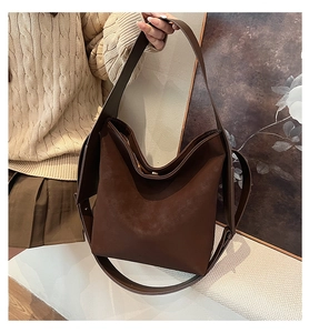 Macro detail of dark brown leather bucket bag showing wide strap and matte texture