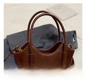 Detalle de bolso de mano de cuero marrón oscuro con asa redonda y cremalleras de metal oro