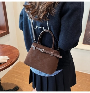 Detail of dark brown suede handbag with decorative buckle and cylinder handle in style
