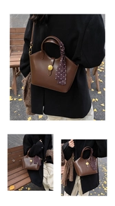 Sac fourre-tout en cuir marron avec ornement doré et foulard à pois sur un banc en bois