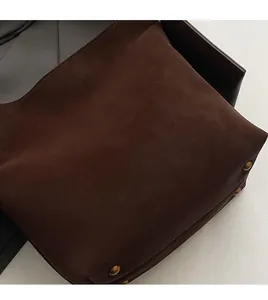 Close-up of brown matte leather bucket bag with metallic rivet detail and logo